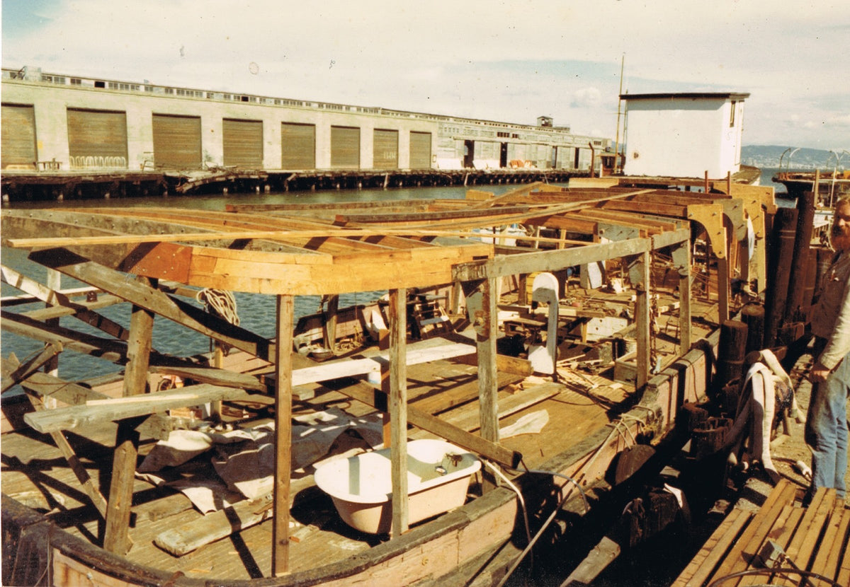 The Lansdown Arts floating studio under restoration on San Francisco Bay, showing the reclaimed boat’s exposed timber framework.