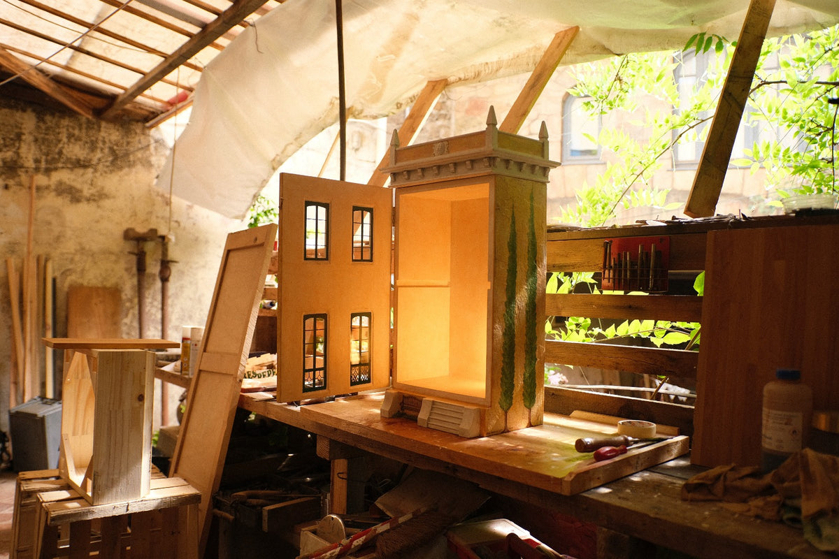 Open interior of the handmade Piccolo Toscano dollhouse in Eric Lansdown’s French workshop, with its hinged façade revealing an illuminated display space.