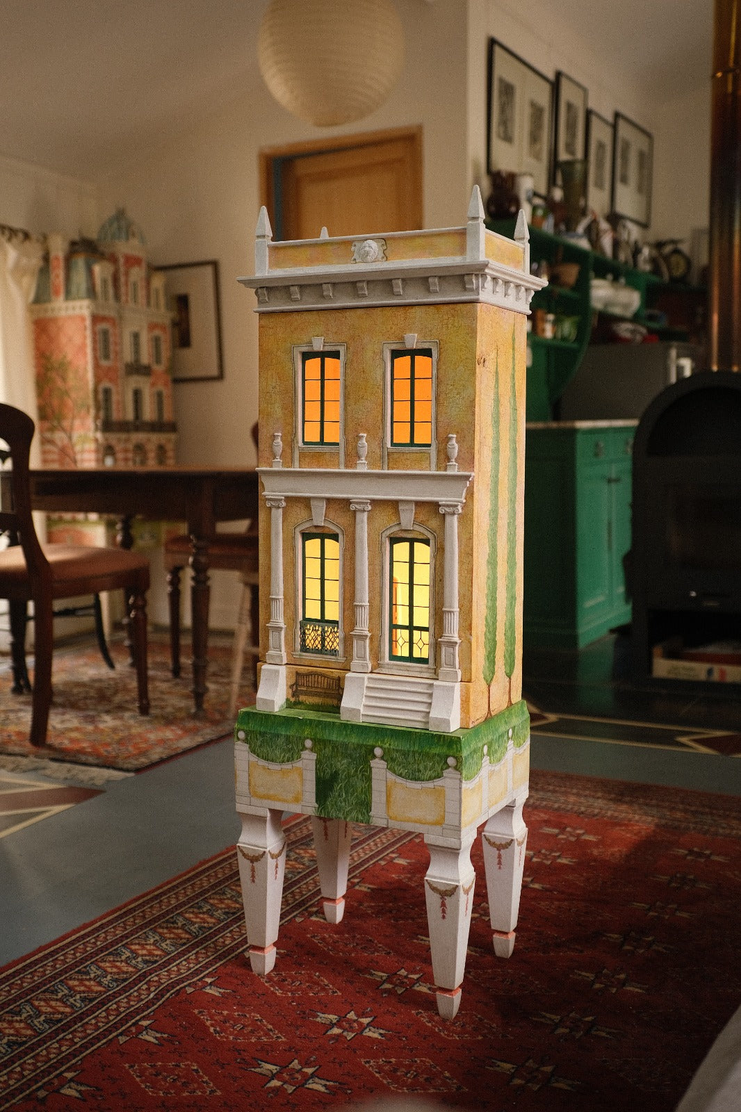 Three-quarter view of Piccolo Toscano, a handcrafted Tuscan dollhouse with an illuminated façade, hand-painted cypress trees and a sculptural furniture-style base.
