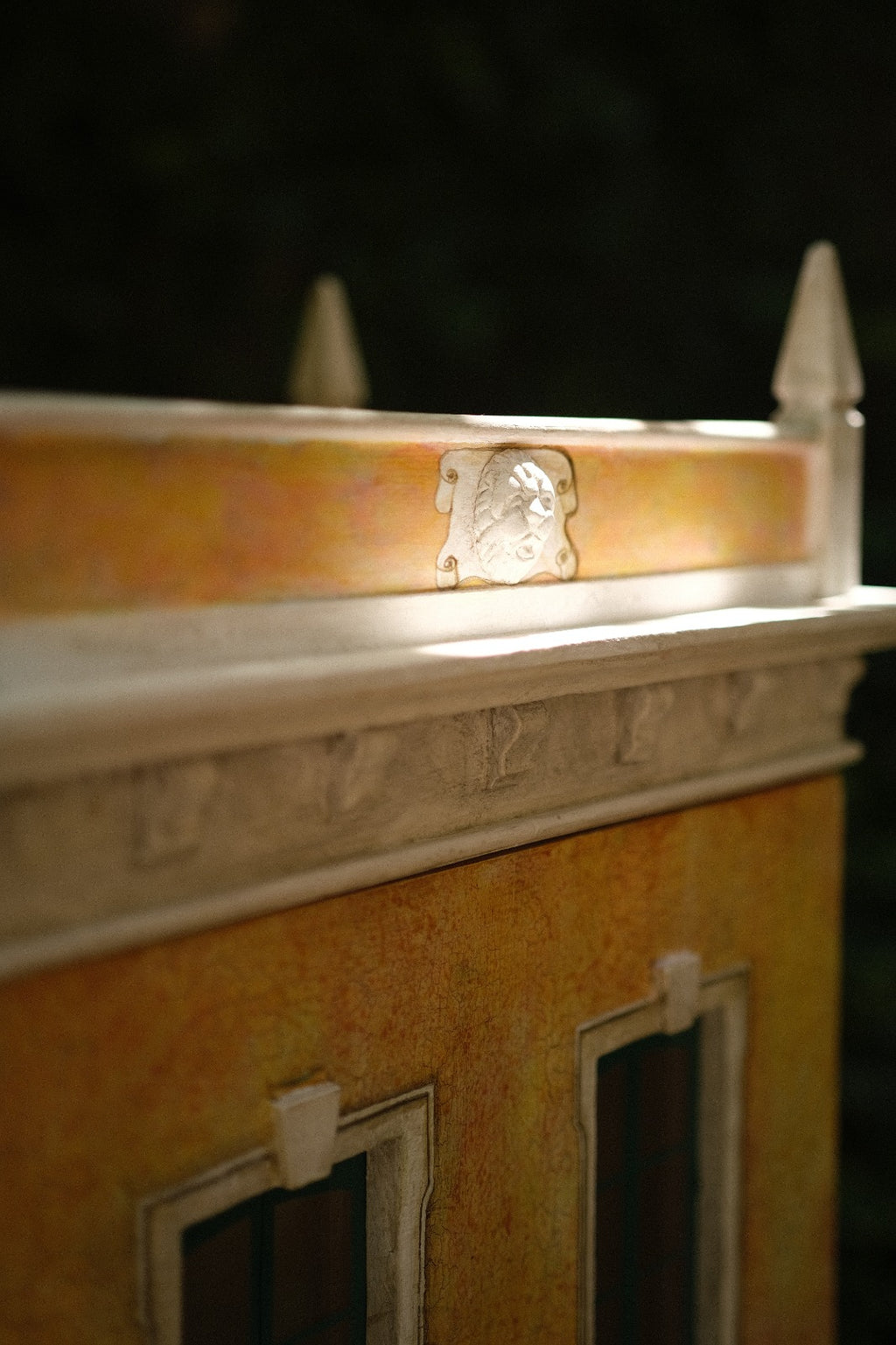 Classical cornice, miniature crest and hand-aged ochre finish on Piccolo Toscano, showing the fine architectural modelmaking of this collectible dollhouse.