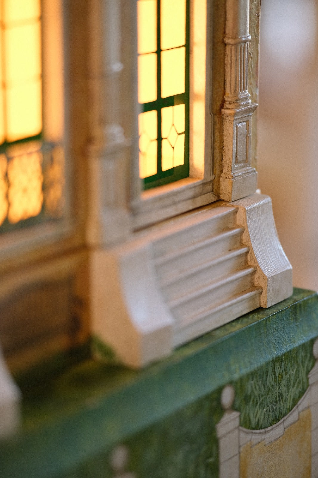 Artistic close-up of illuminated green-trimmed windows and entrance steps on Cypress House, a handmade miniature dollhome