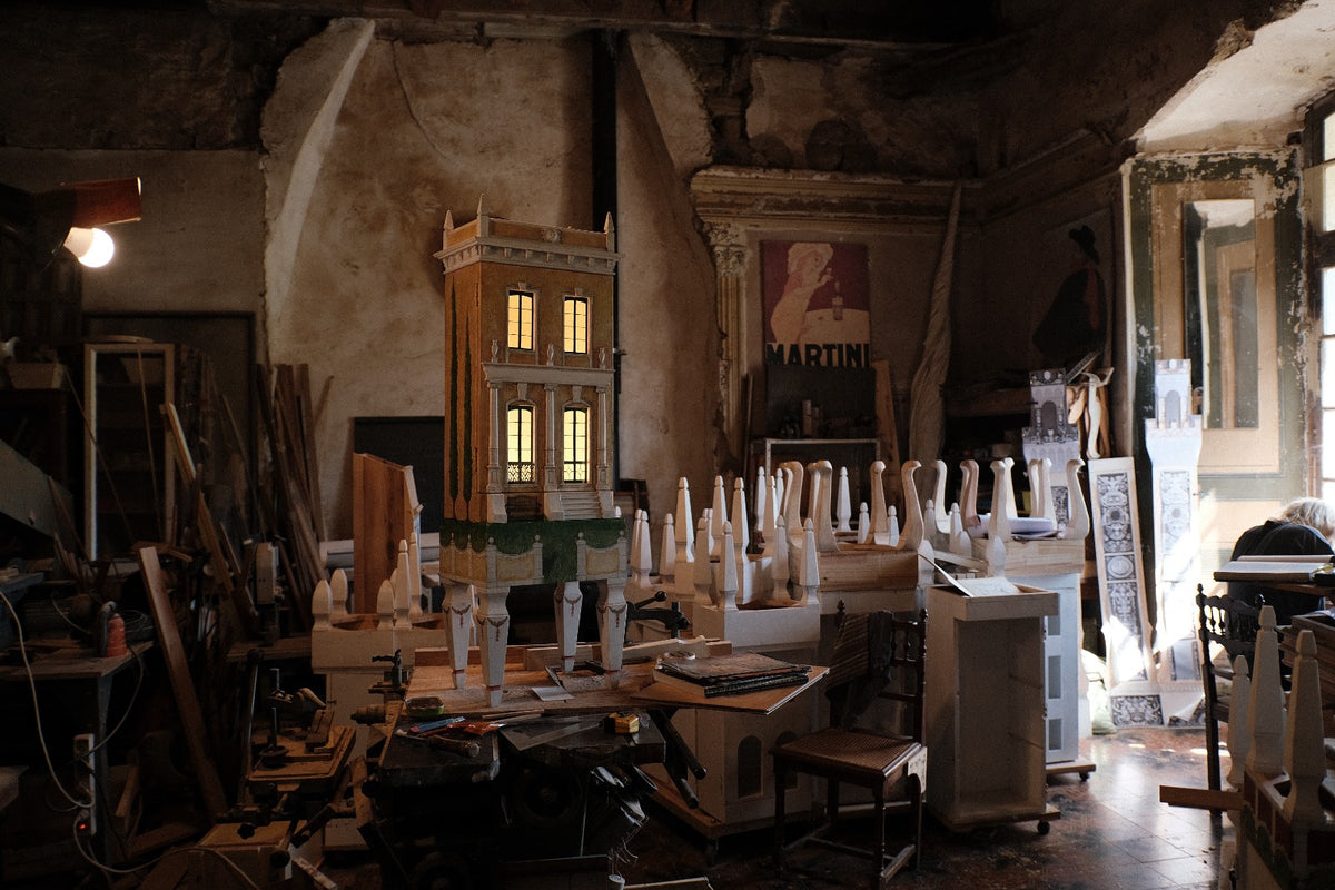 Illuminated Piccolo Toscano architectural dollhouse on Eric Lansdown’s workbench in southern France, surrounded by tools and handcrafted components.