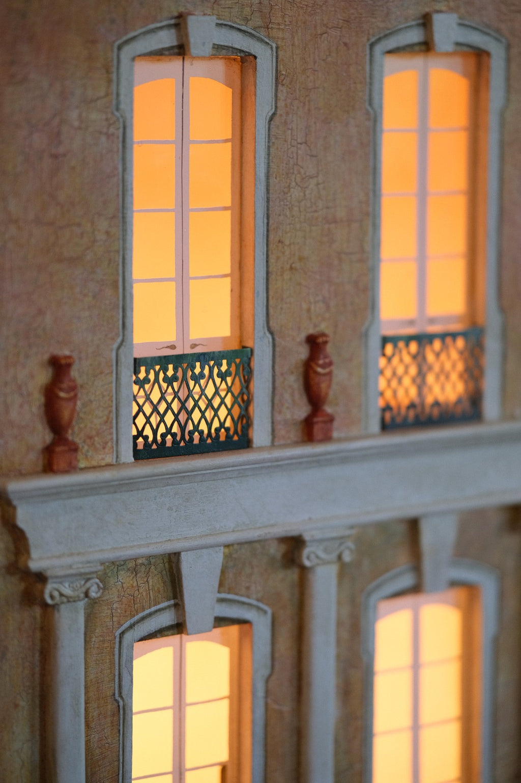 Illuminated French windows and ornate metal balcony detail on Cypress House, a handcrafted luxury architectural dollhouse