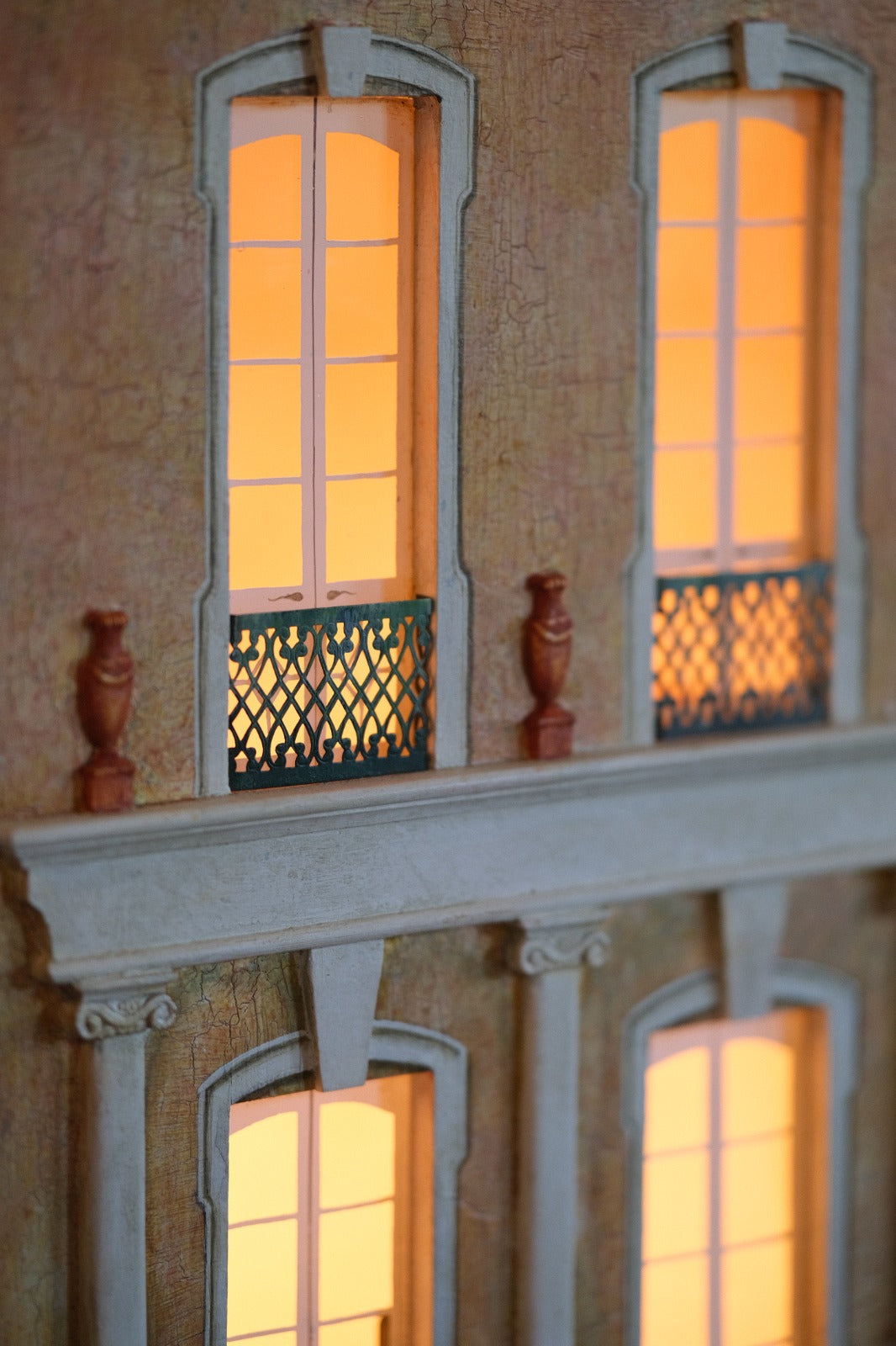 Illuminated French windows and ornate metal balcony detail on Cypress House, a handcrafted luxury architectural dollhouse