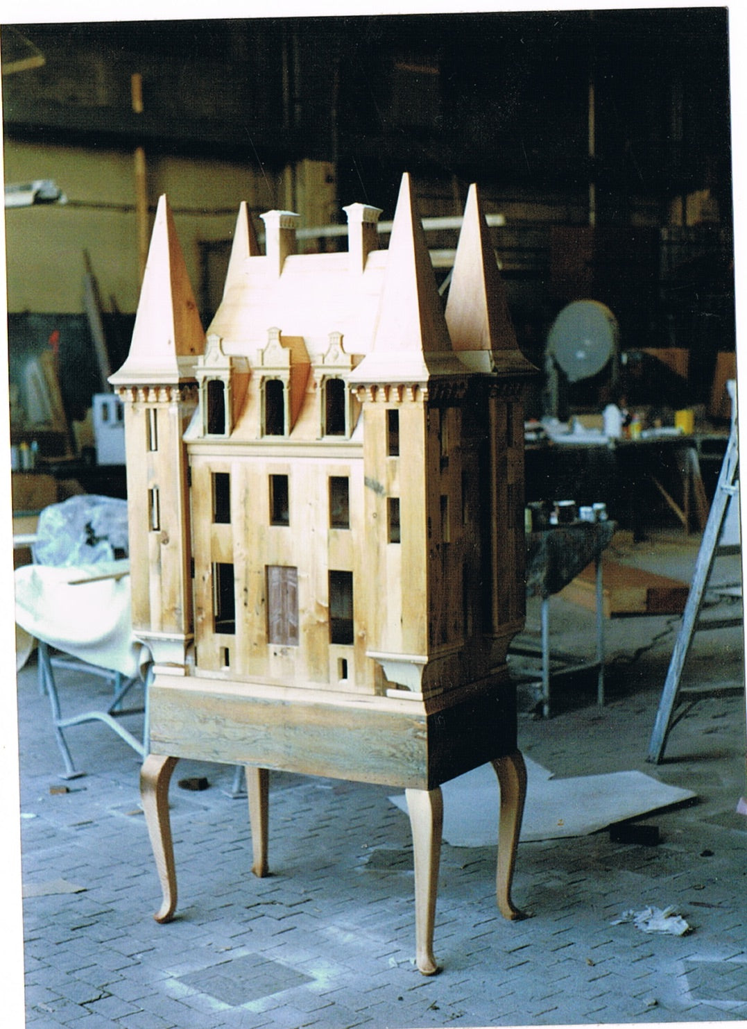 Handmade French château dollhouse under construction in the Lansdown Arts studio, showing its unfinished timber façade and architectural details.