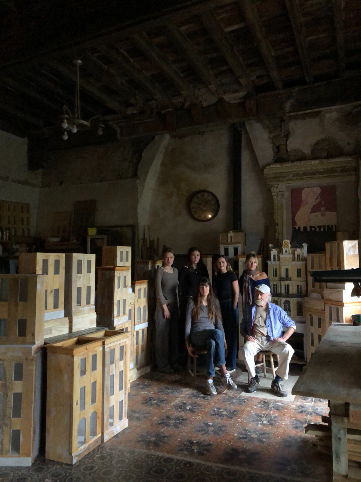 Eric Lansdown with young artists and apprentices among unfinished architectural dollhouses in the Gabian studio, passing traditional craftsmanship to a new generation.